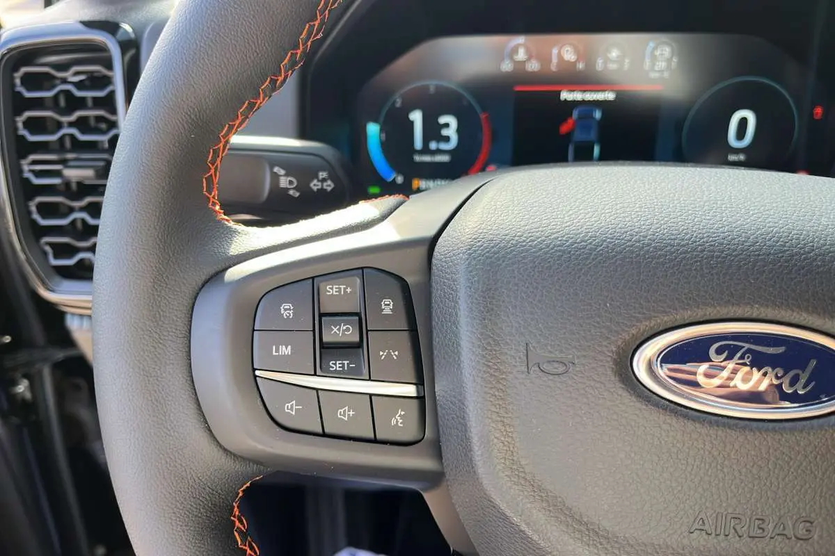 Gros plan sur le volant cuir noir avec surpiqûres orange du Ford Ranger Wildtrak 2026, affichage numérique en arrière-plan.