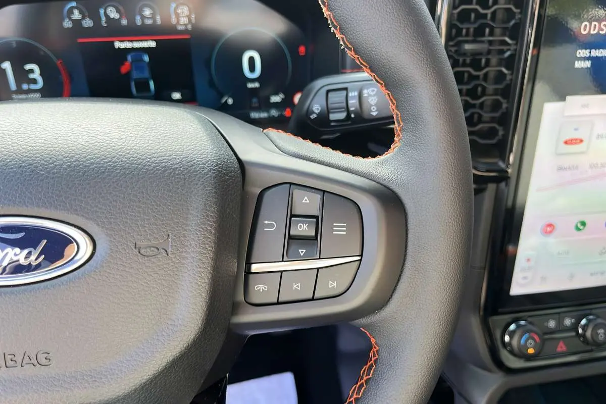 Gros plan sur le volant cuir noir avec surpiqûres orange du Ford Ranger Wildtrak 2026, tableau de bord et écran tactile visibles.