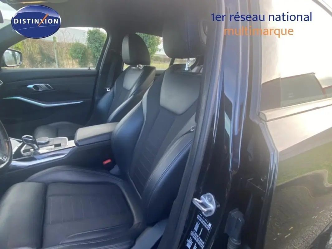 Vue intérieure côté conducteur de la BMW Série 3 G20 noire, mettant en valeur les sièges sport en cuir et l'accoudoir central.