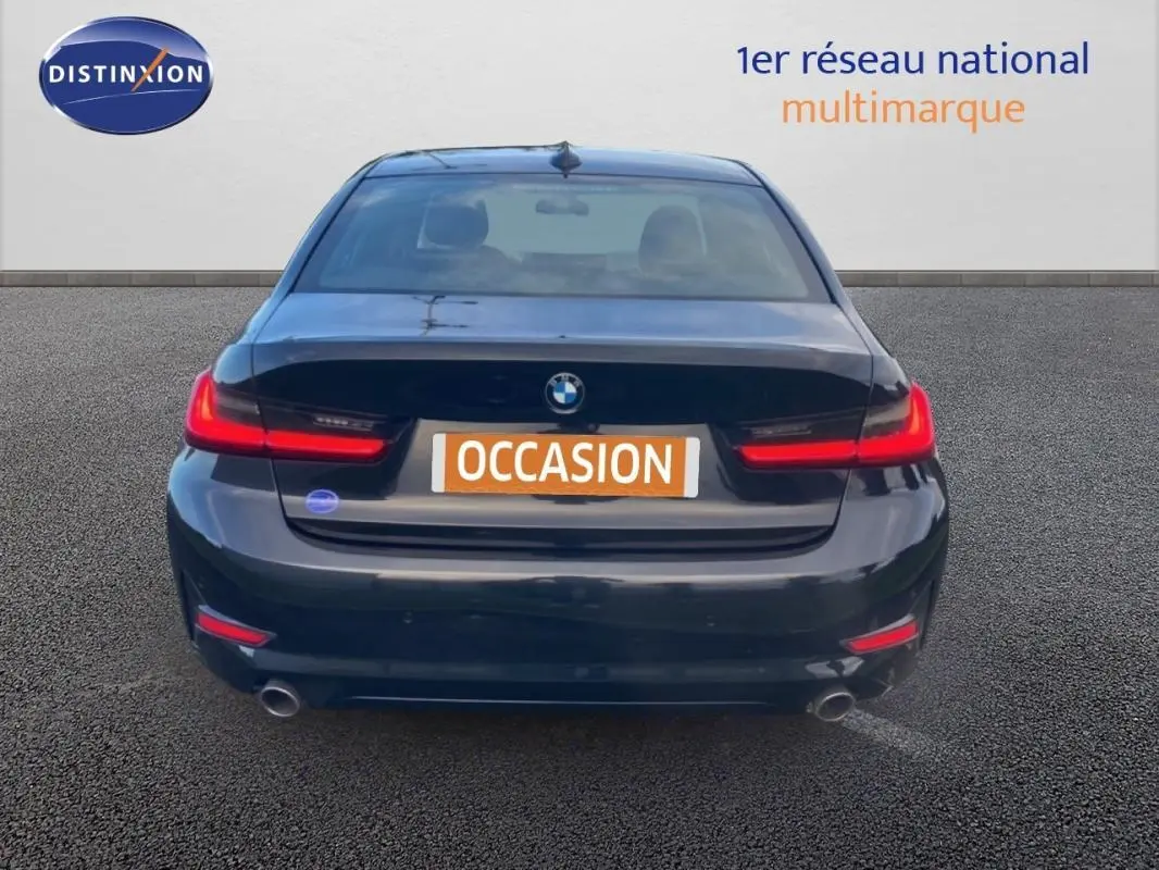 Vue arrière d'une BMW Série 3 G20 noire de 2019 avec feux arrière allumés et double sortie d'échappement.