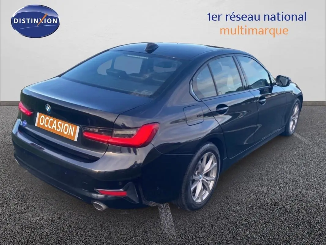 BMW Série 3 G20 noire vue 3/4 arrière droit, avec jantes alliage 17 pouces et feux arrière allumés.