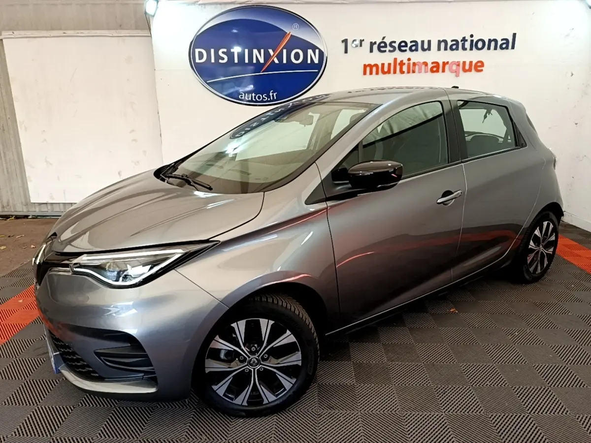 Renault ZOE gris clair en 3/4 avant droit, avec jantes alliage et phares LED, en intérieur showroom.