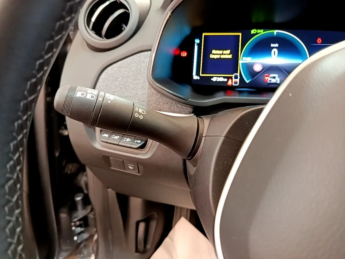 Gros plan sur la manette de clignotant à gauche du volant, avec le combiné d'instruments numérique éclairé de la Renault ZOE gris clair.