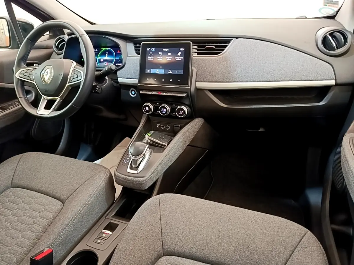 Vue intérieure avant de la Renault ZOE gris clair, montrant le tableau de bord avec écran tactile central et volant multifonctions.