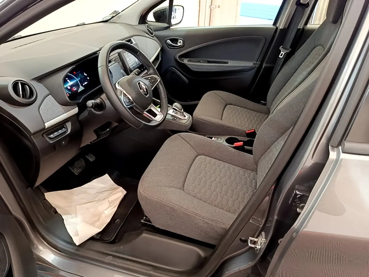 Vue intérieure côté conducteur de la Renault ZOE gris clair, montrant les sièges tissu et le tableau de bord avec écran tactile.
