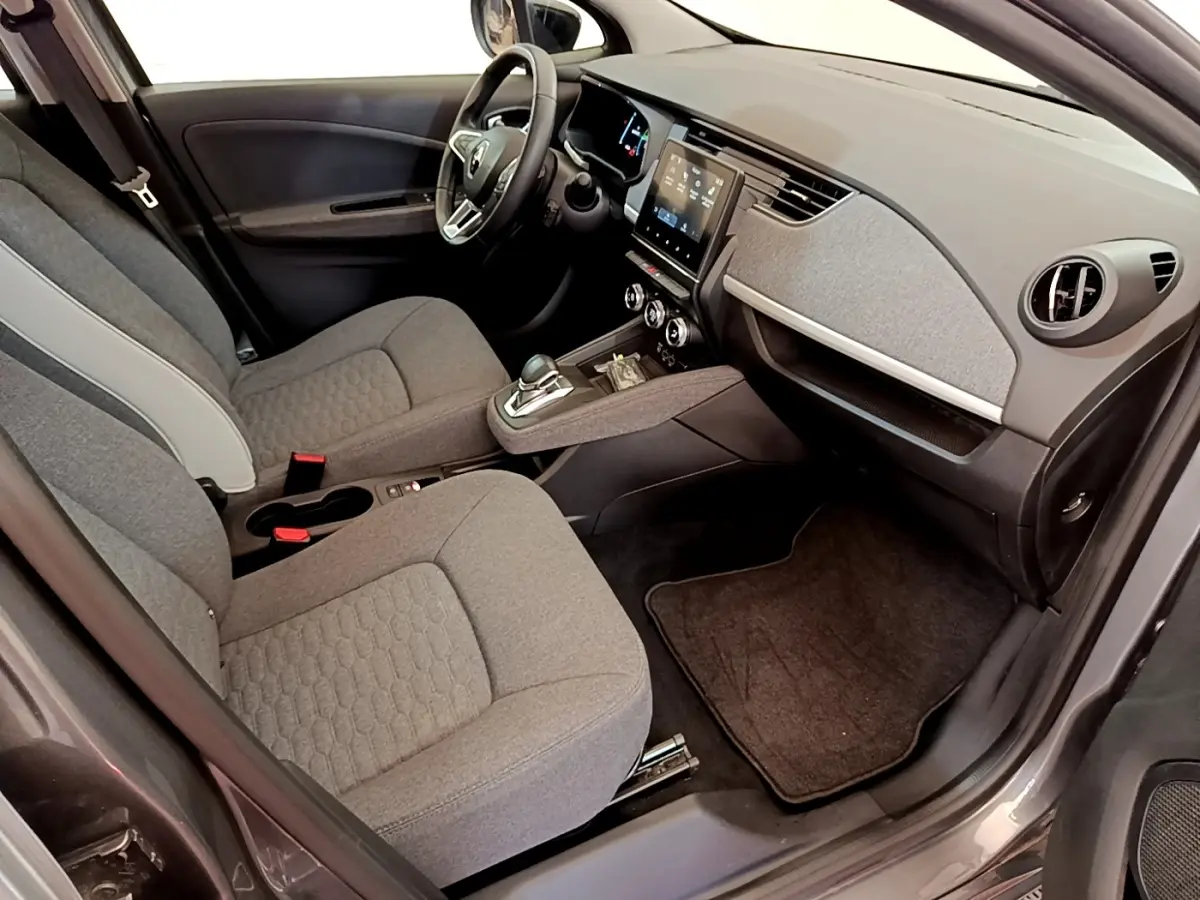 Vue intérieure côté conducteur de la Renault ZOE gris clair, mettant en valeur le tableau de bord et l’écran tactile central.