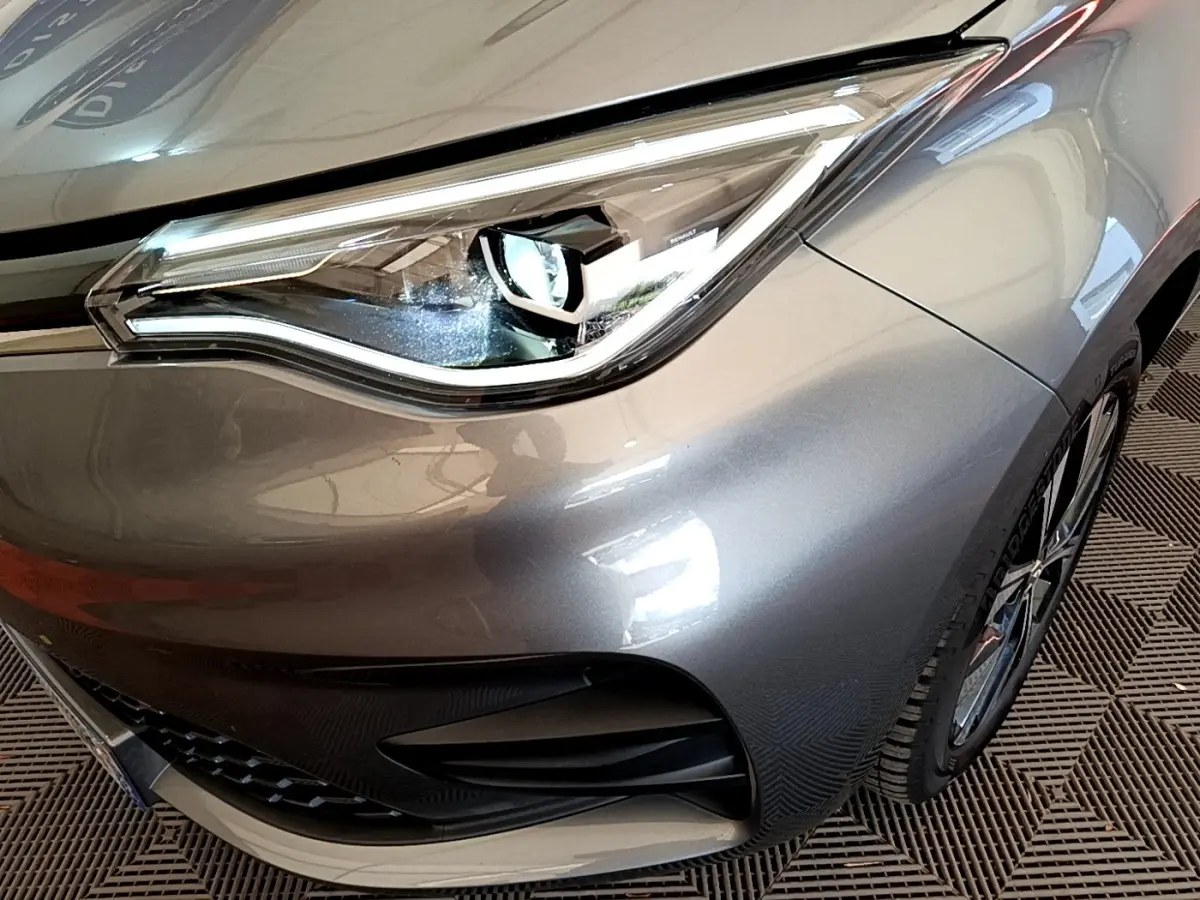 Gros plan sur le phare avant droit de la Renault ZOE gris clair, mettant en valeur le design LED et la calandre.
