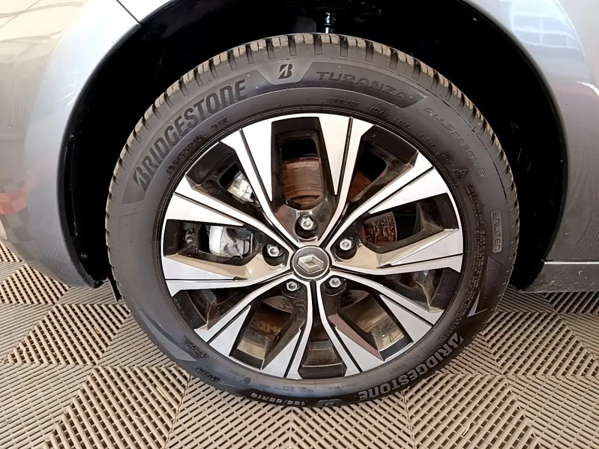 Gros plan sur la roue avant droite d’une Renault ZOE gris clair, jante alliage à design moderne avec logo Renault central.