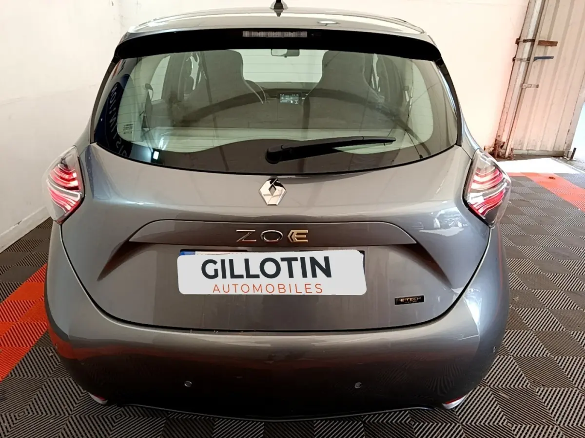 Vue arrière d'une Renault ZOE gris clair avec feux LED et logo ZOE E-Tech visible sur un sol à damier noir et rouge.