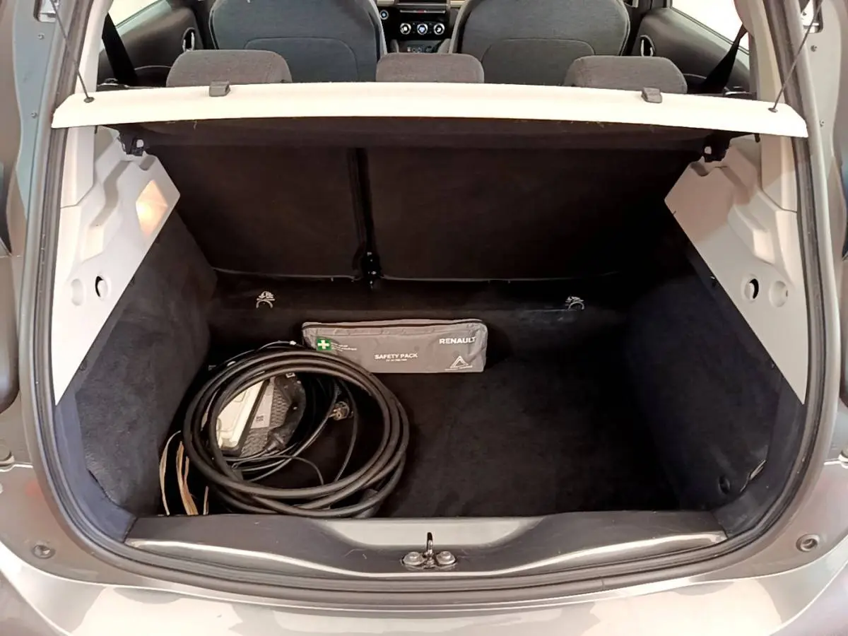 Coffre ouvert d’une Renault ZOE gris clair vue arrière, avec câble de charge et trousse de sécurité visibles.