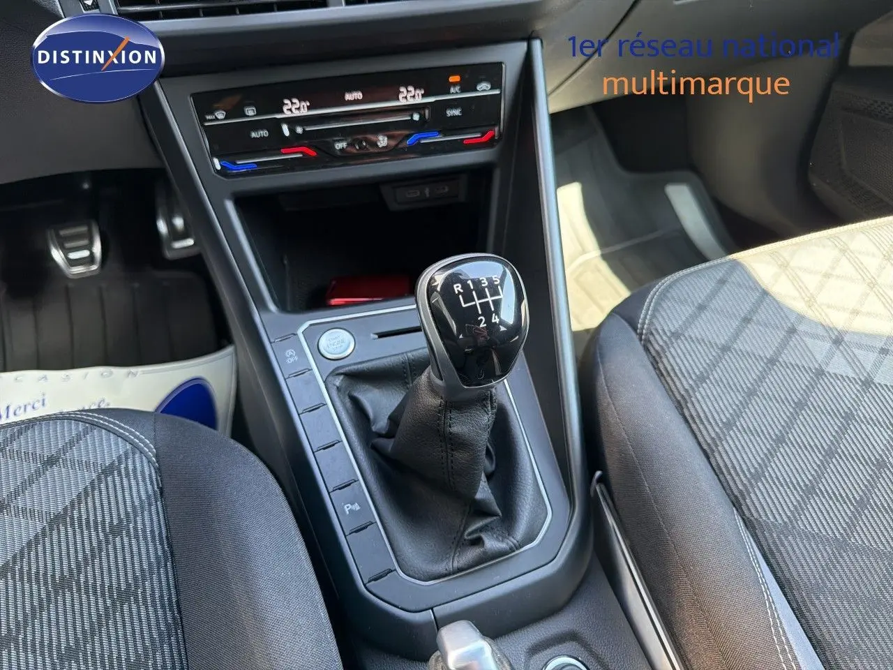 Vue intérieure centrée sur la console centrale d'une Volkswagen Polo rouge Roi 2023 avec levier de vitesse manuel et climatisation digitale.