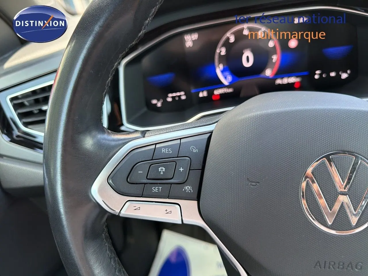 Gros plan sur le volant multifonction noir avec logo Volkswagen, tableau de bord numérique flou en arrière-plan.
