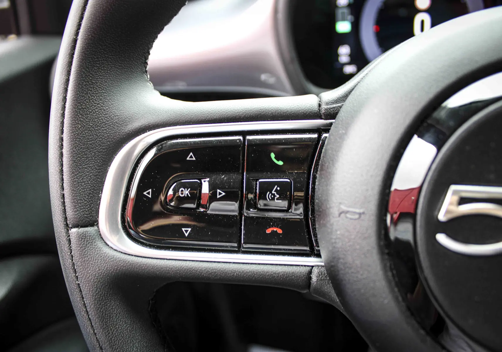 Gros plan sur les commandes gauche du volant noir de la Fiat 500 électrique gris minéral 2023, avec boutons multifonctions.
