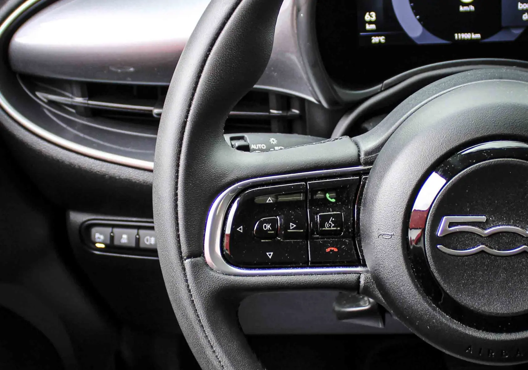 Gros plan sur le volant noir et le tableau de bord numérique de la FIAT 500 électrique 2023, ambiance intérieure moderne.