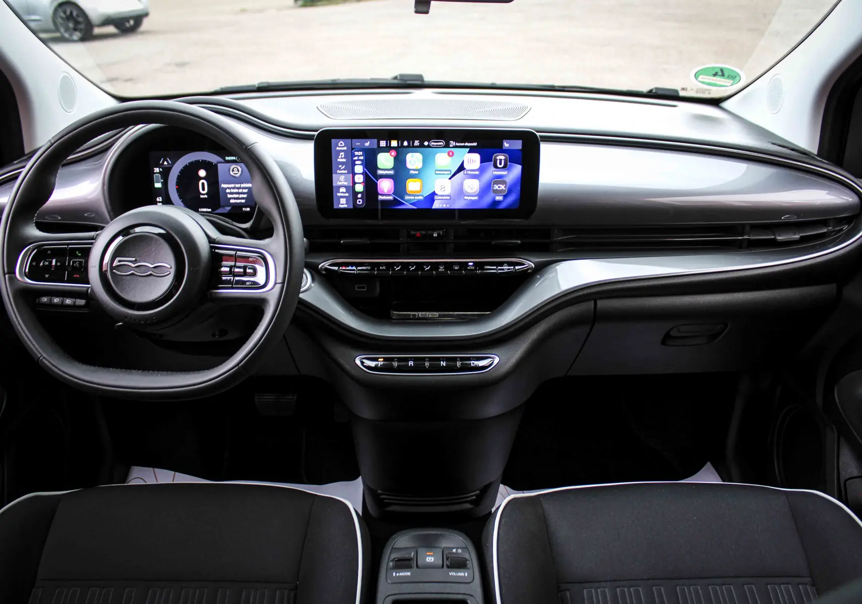 Vue frontale de l’habitacle de la FIAT 500 électrique gris minéral, avec tableau de bord numérique et écran tactile central.