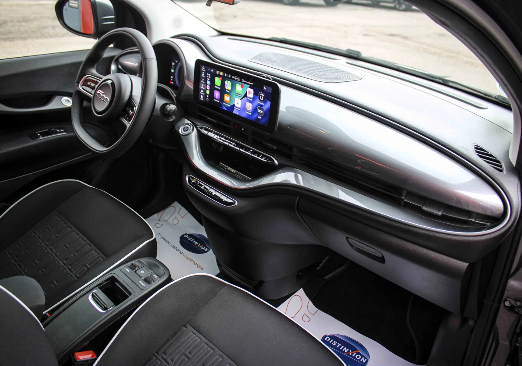 Vue intérieure côté conducteur de la Fiat 500 électrique 2023, tableau de bord gris minéral métal avec écran tactile et sièges noirs.
