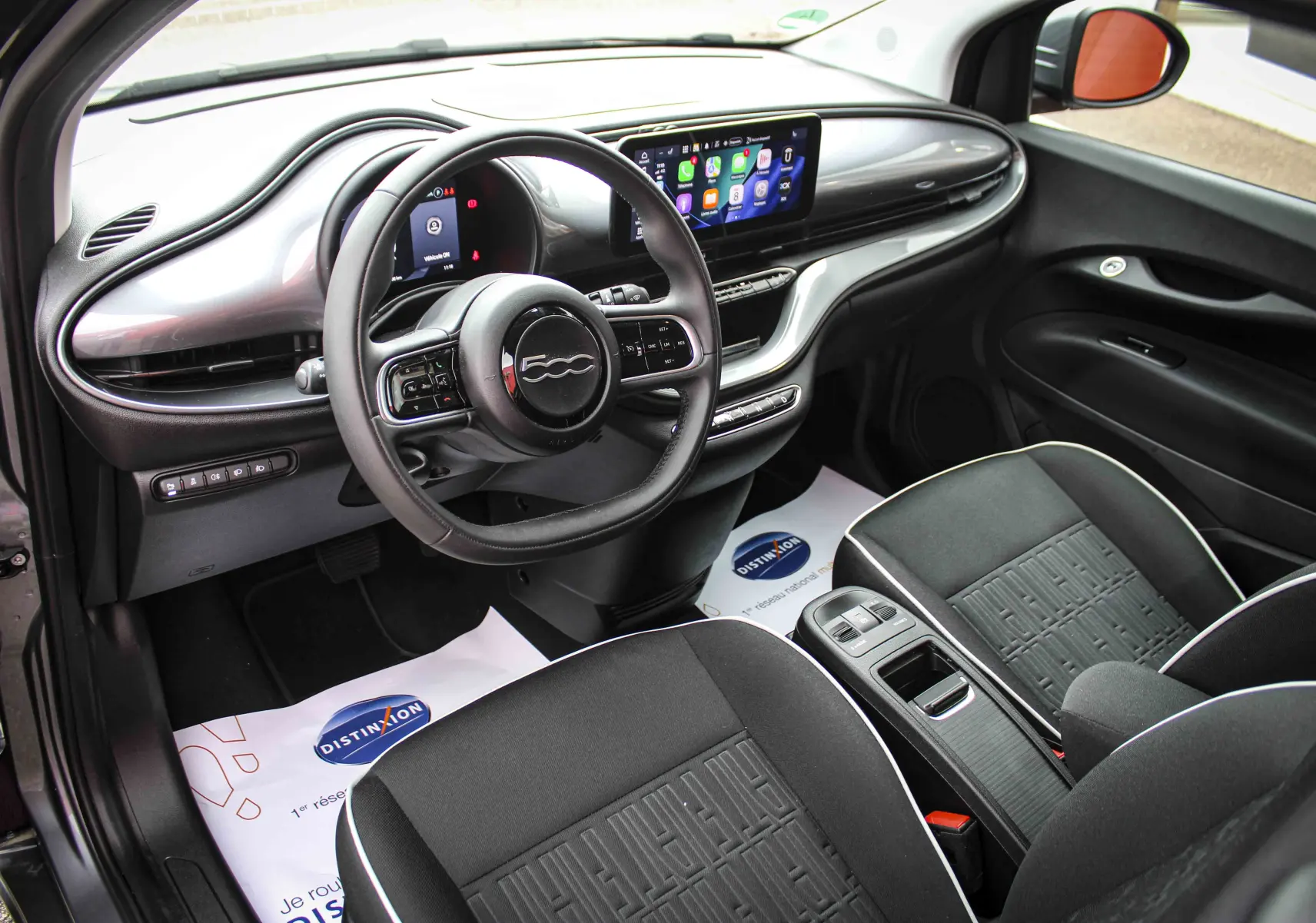 Vue intérieure côté conducteur de la Fiat 500 électrique 2023, avec tableau de bord noir et écran tactile central.
