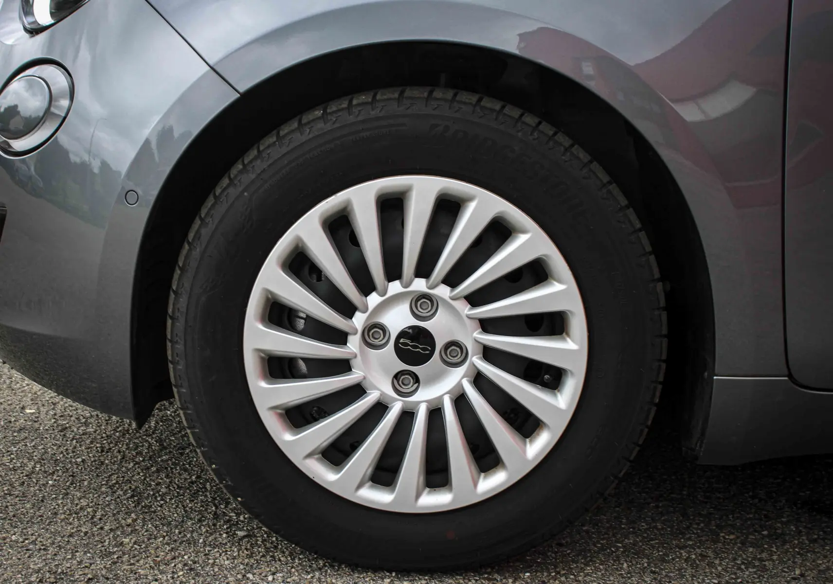 Gros plan sur la roue avant gauche d'une FIAT 500 électrique gris minéral métal avec jante argentée à rayons fins.