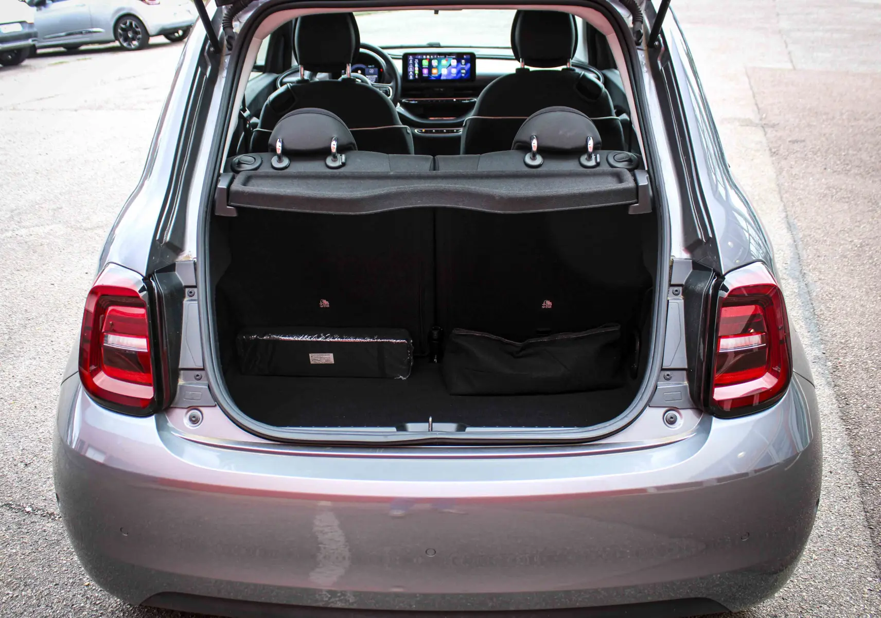 Vue arrière ouverte sur le coffre d'une FIAT 500 électrique gris minéral métal, avec intérieur noir et sièges visibles.