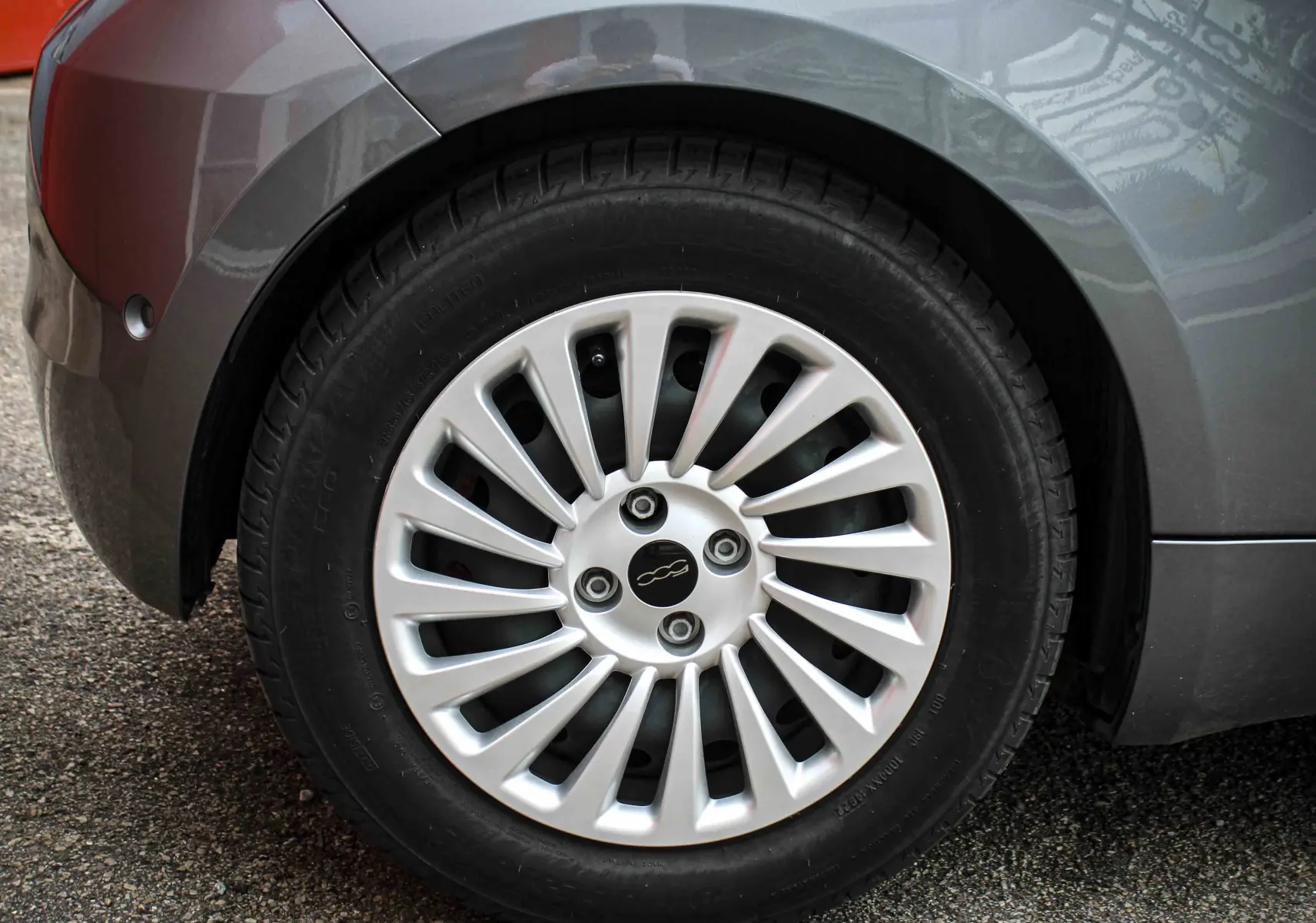 Gros plan sur la roue arrière gauche d'une FIAT 500 électrique gris minéral métal avec jante argentée à rayons fins.