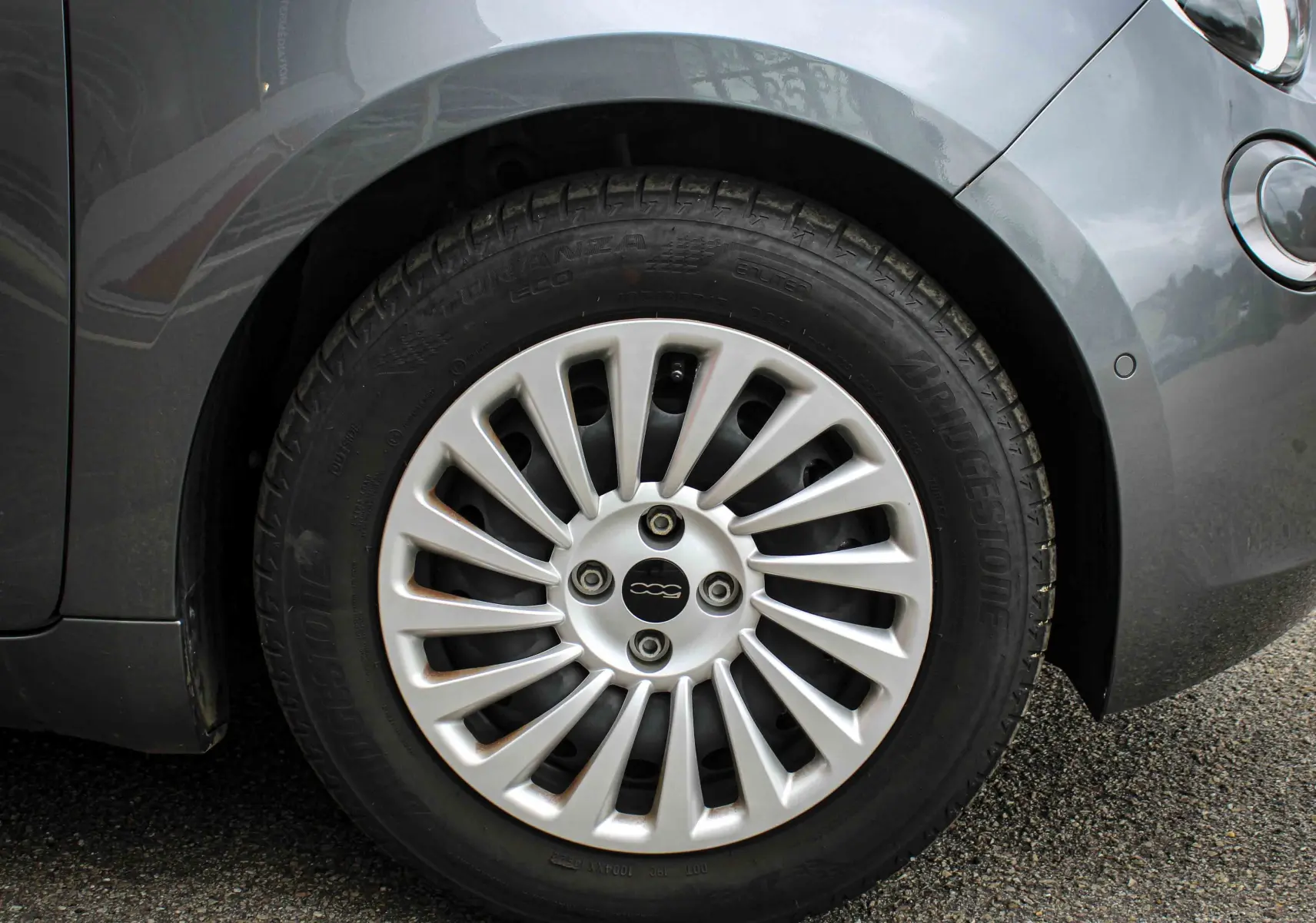 Gros plan sur la roue avant droite d'une Fiat 500 électrique gris minéral métal avec jante argentée stylisée.