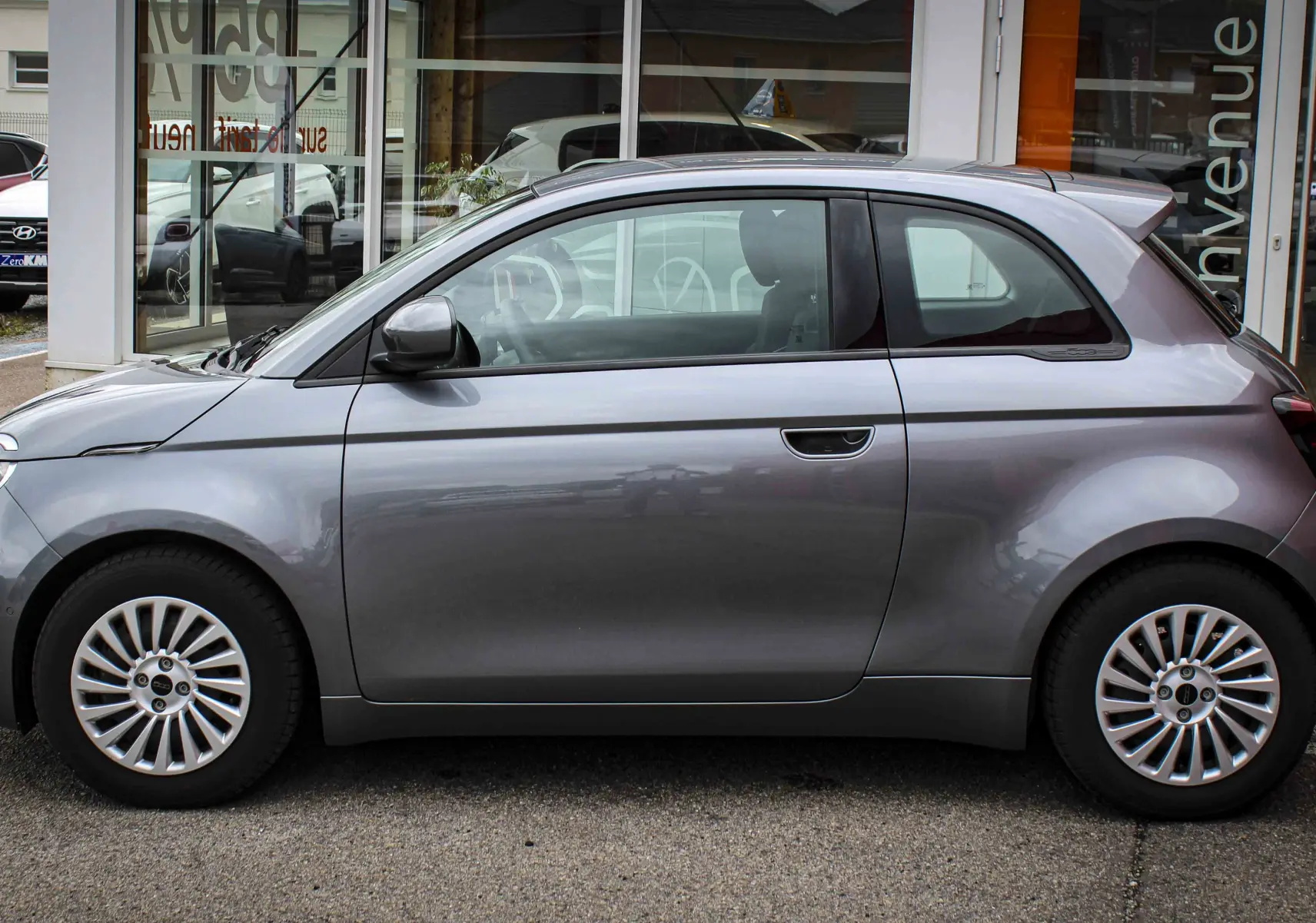 Profil côté gauche de la Fiat 500 électrique 2023 gris minéral métal, avec jantes multibranches et lignes arrondies.