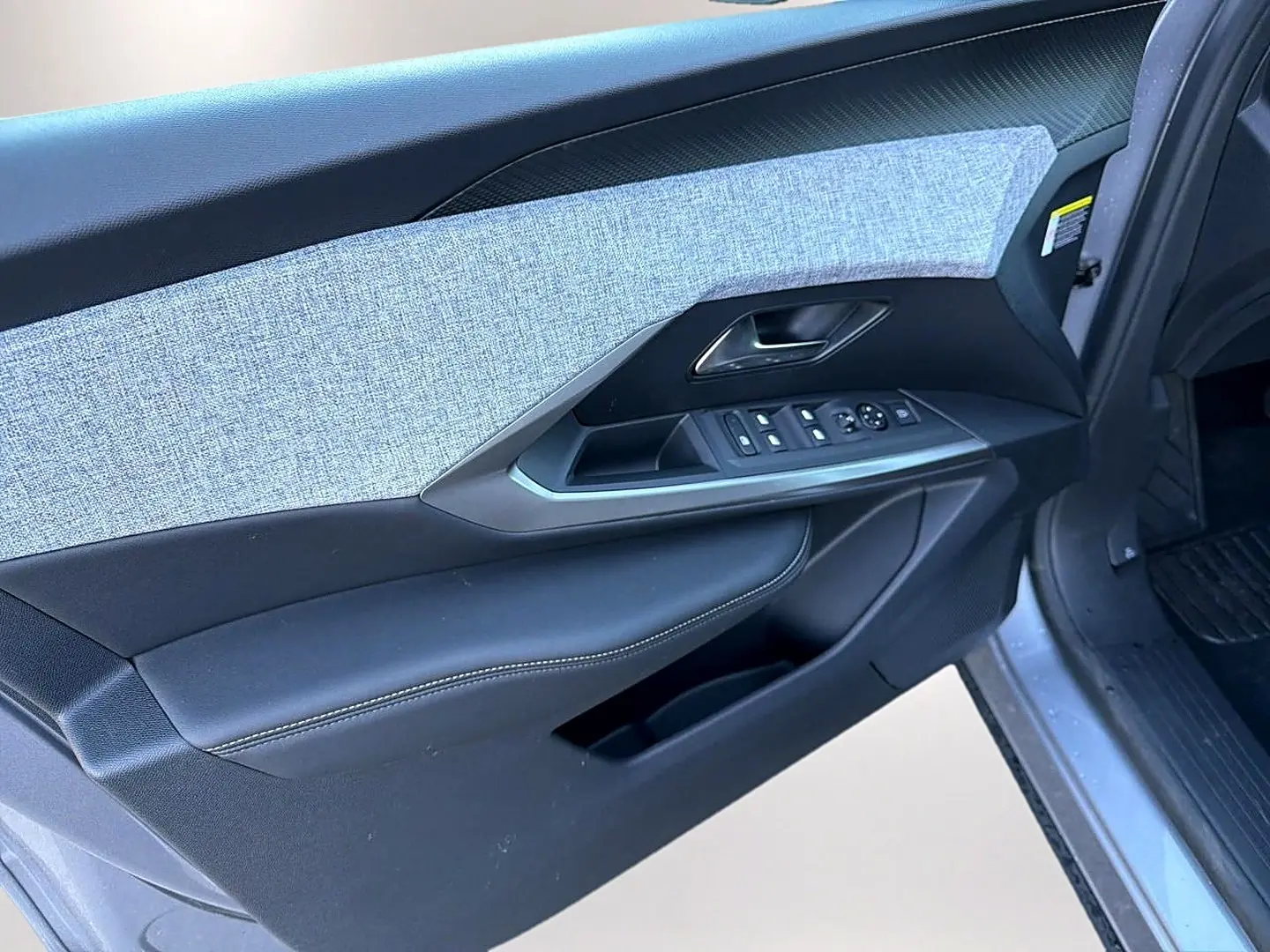 Vue rapprochée de la porte avant gauche du Peugeot 5008 gris artense, montrant les commandes des vitres et le revêtement tissu et cuir.