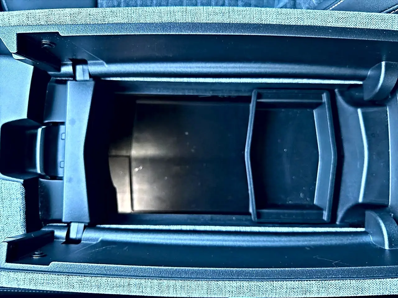 Vue rapprochée de l'accoudoir central ouvert du Peugeot 5008 gris Artense, montrant le rangement intérieur noir.