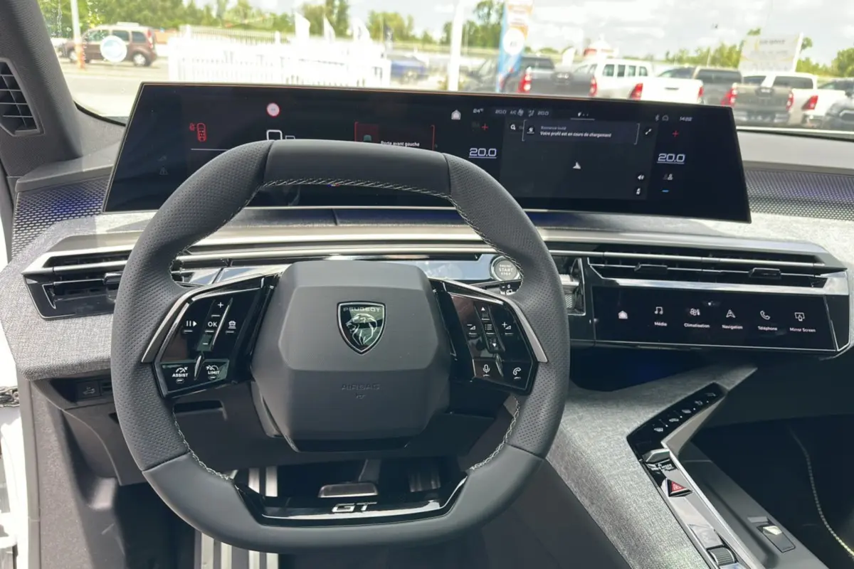 Vue intérieure centrée sur le volant cuir multifonctions et le tableau de bord numérique du Peugeot 5008 Hybrid GT.