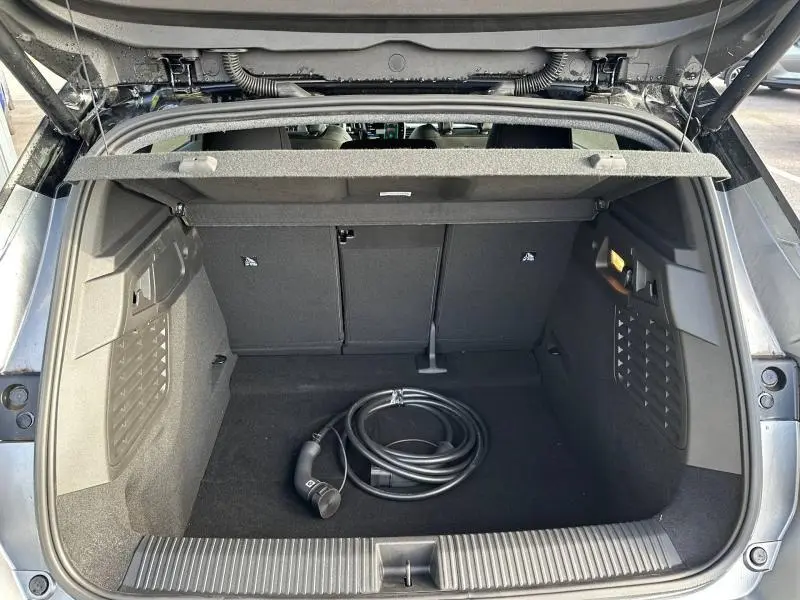 Coffre ouvert vu de l'arrière d'un Renault Scenic gris schiste avec câble de recharge électrique enroulé au centre.
