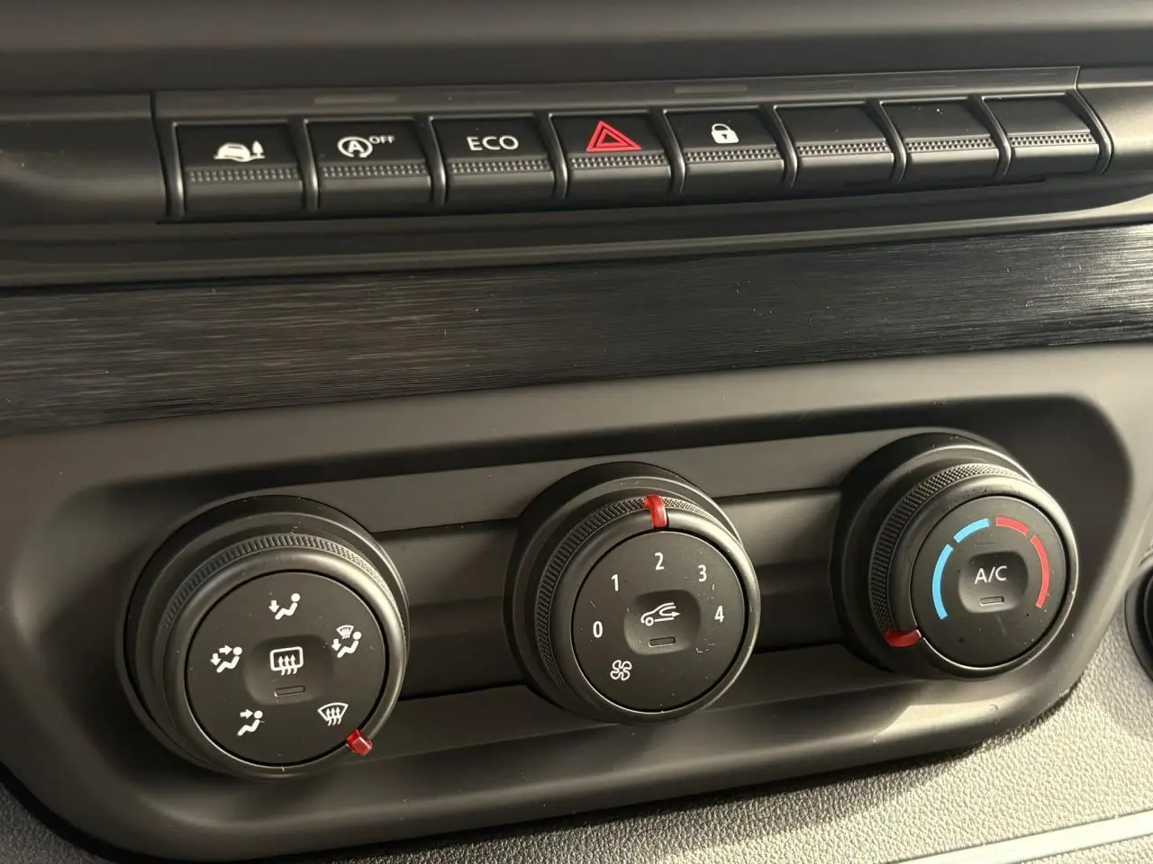 Gros plan sur les commandes de climatisation noires du Renault Trafic Fourgon blanc Glacier, avec habillage bois visible.