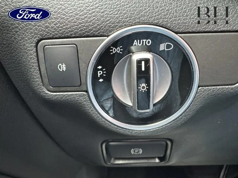 Gros plan sur la commande des phares et bouton de frein de stationnement dans un intérieur noir de Mercedes GLA 180 d Fascination 2018.