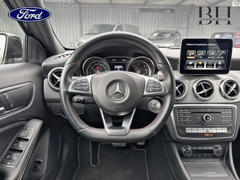 Vue intérieure du tableau de bord et volant cuir noir du Mercedes GLA 180 d Fascination 2018 avec écran multifonction et aérateurs ronds chromés.