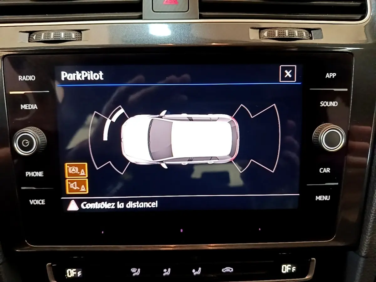 Écran tactile intérieur montrant le système ParkPilot de la Volkswagen Golf noire, vue de dessus du véhicule en blanc.