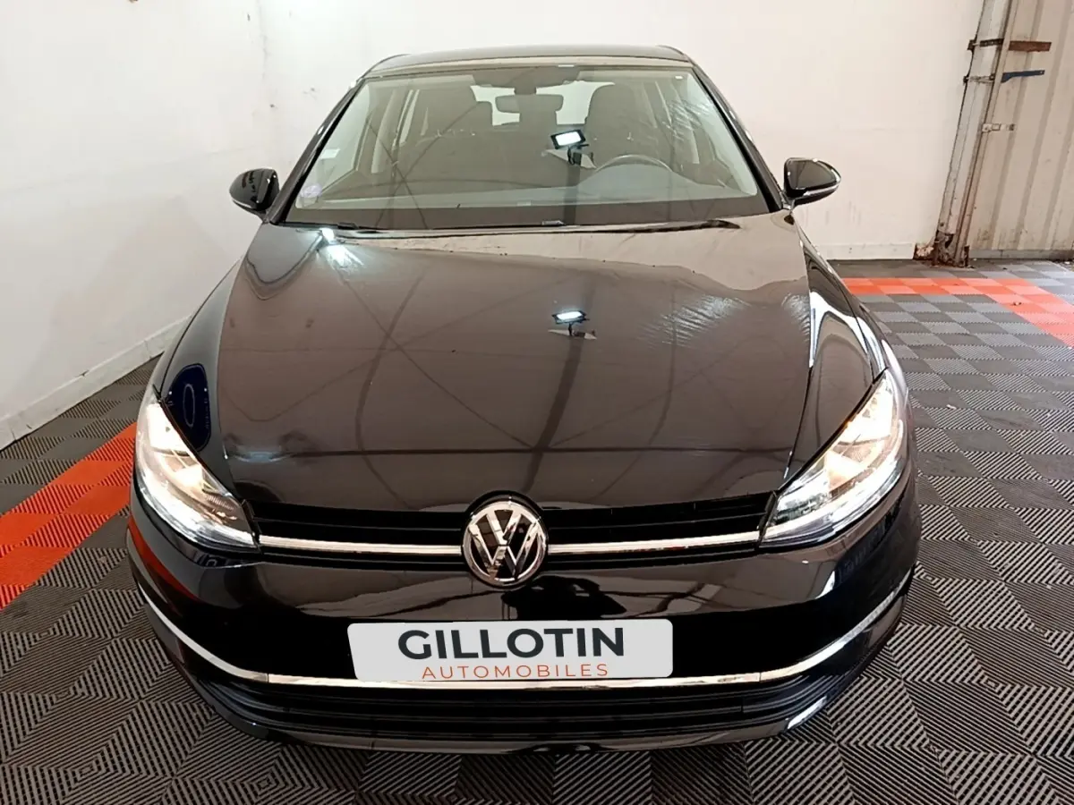 Vue avant d'une Volkswagen Golf noire 2019 avec phares allumés dans un garage fermé.