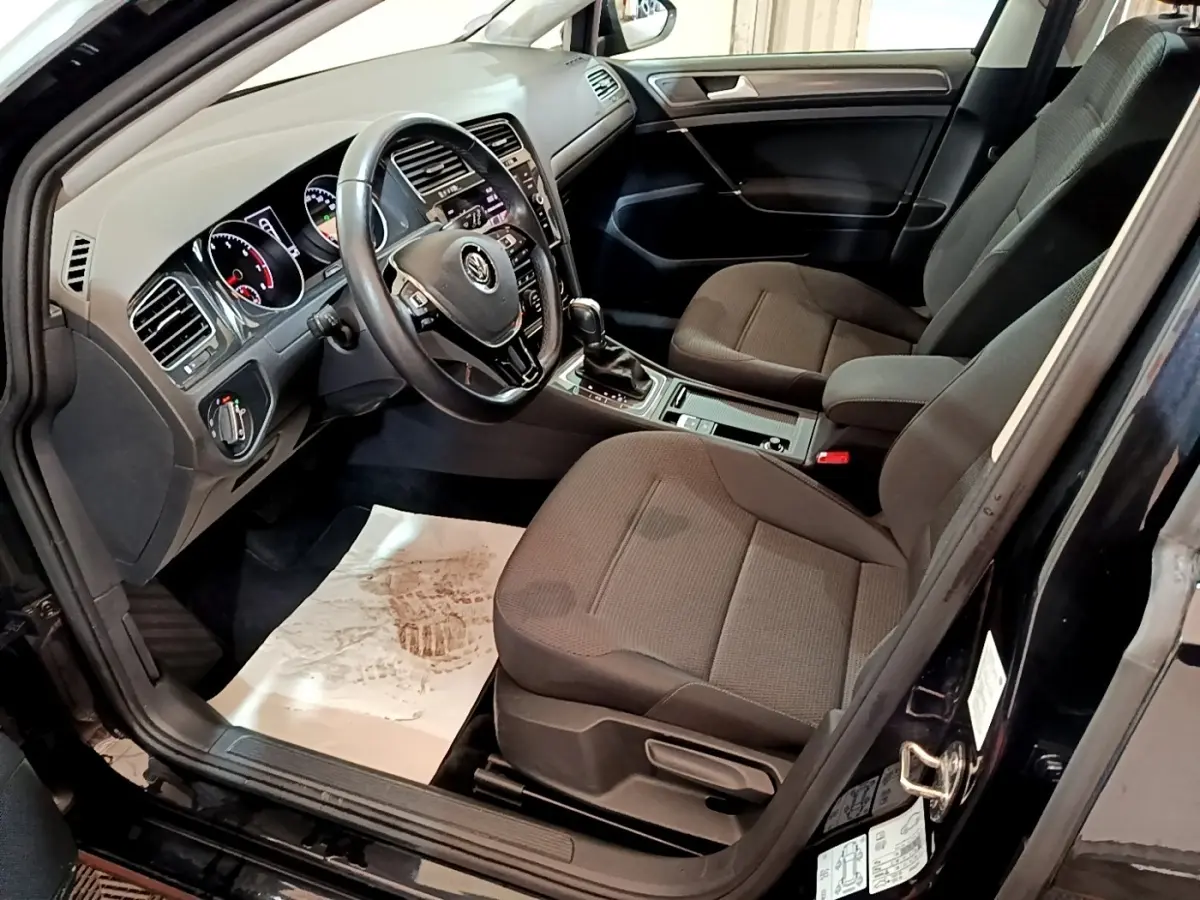 Vue intérieure côté conducteur d'une Volkswagen Golf noire avec volant cuir multifonctions et sièges tissu gris.