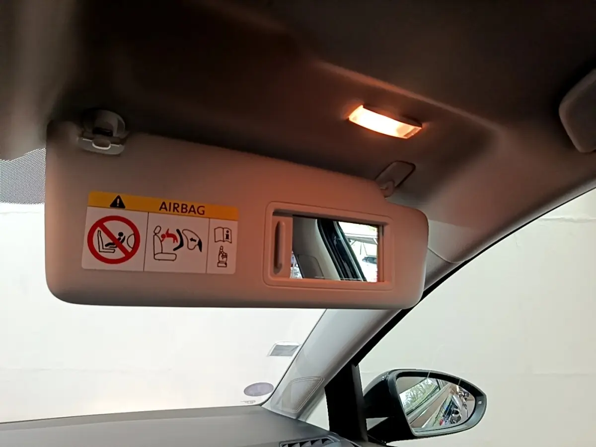 Vue intérieure côté conducteur sur le pare-soleil beige avec miroir et avertissement airbag, rétroviseur noir visible.