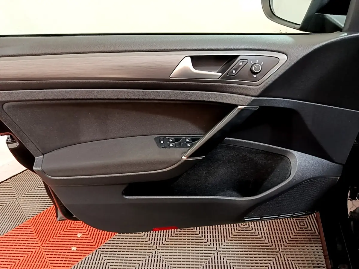 Vue intérieure du panneau de porte avant gauche de la Volkswagen Golf noire, avec commandes électriques et insert imitation bois.