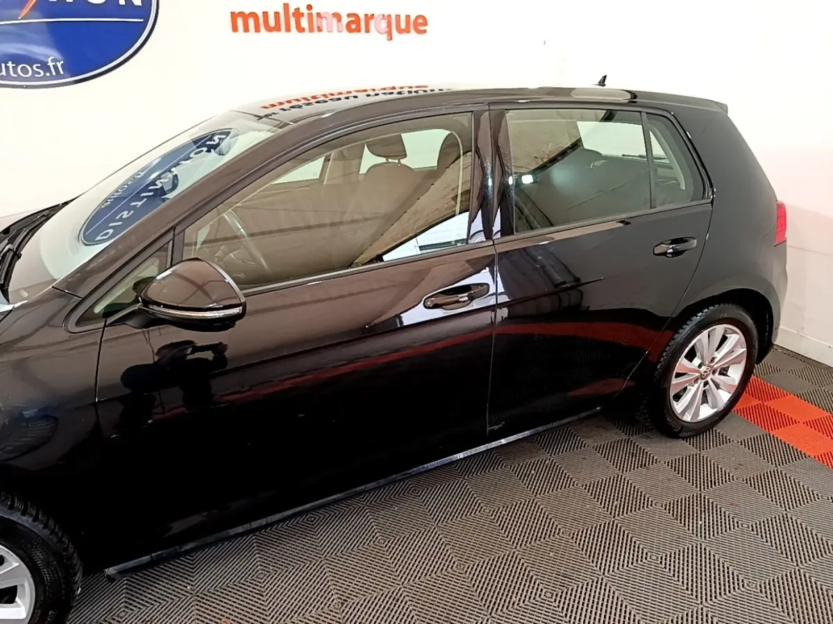 Vue de profil côté gauche d'une Volkswagen Golf noire 2019 stationnée sur sol damier noir et rouge.