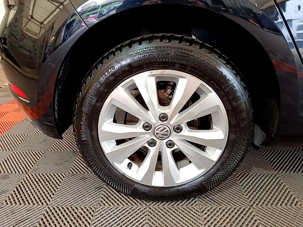 Gros plan sur la roue avant droite d'une Volkswagen Golf noire, avec jante alliage argentée et pneu hiver.