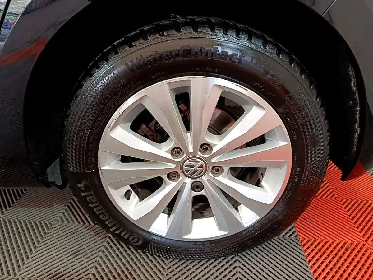 Gros plan sur la roue avant droite noire d'une Volkswagen Golf 1.0 TSI 115 DSG7 avec jante argentée et logo VW.