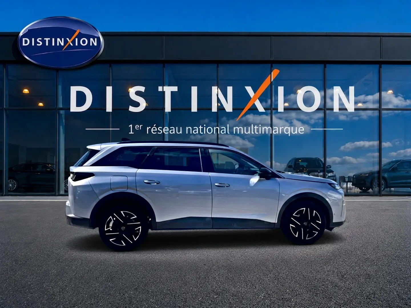 Peugeot 5008 Hybrid 145 allure gris artense en profil droit devant une vitrine Distinxion, jantes alu noires et toit noir.