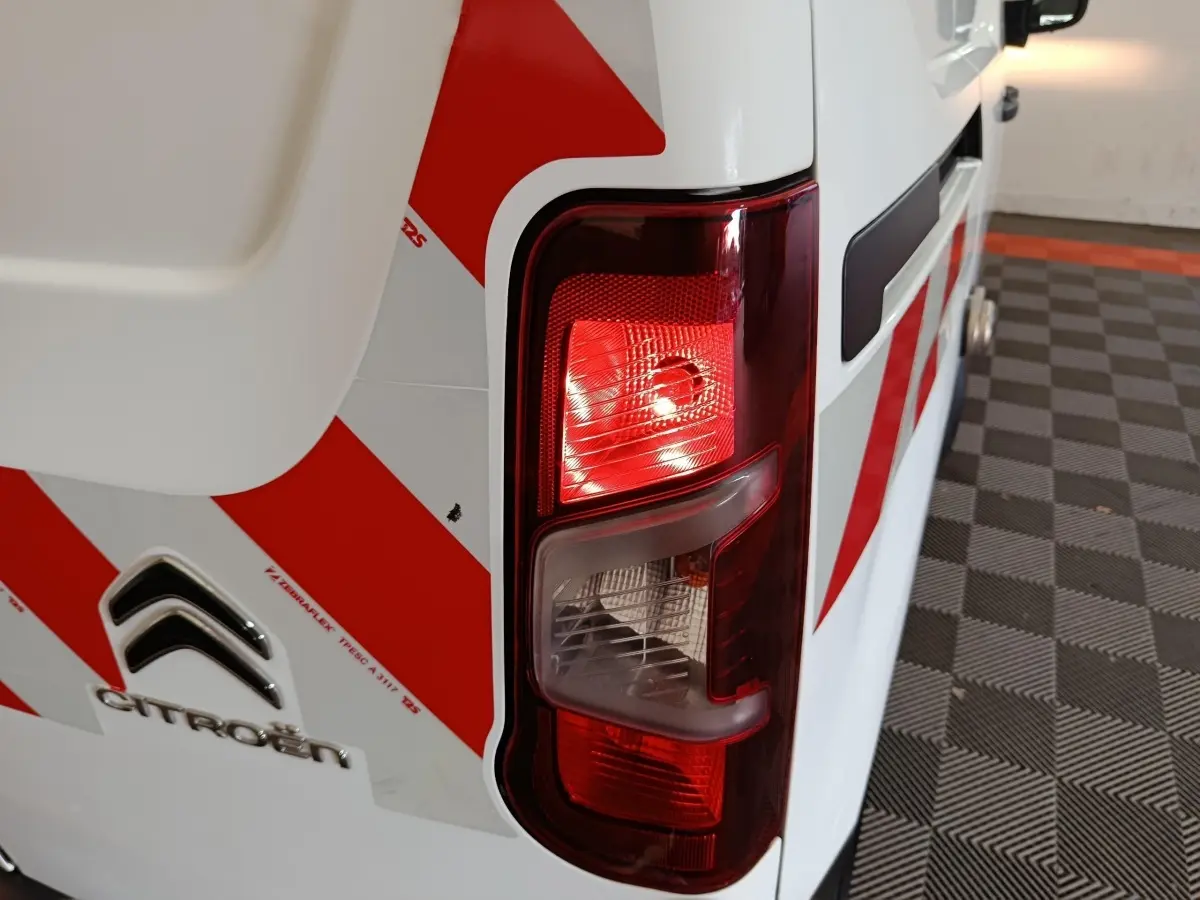 Gros plan sur le feu arrière droit d’un Citroën Berlingo blanc 2021 avec marquages rouges en diagonale.