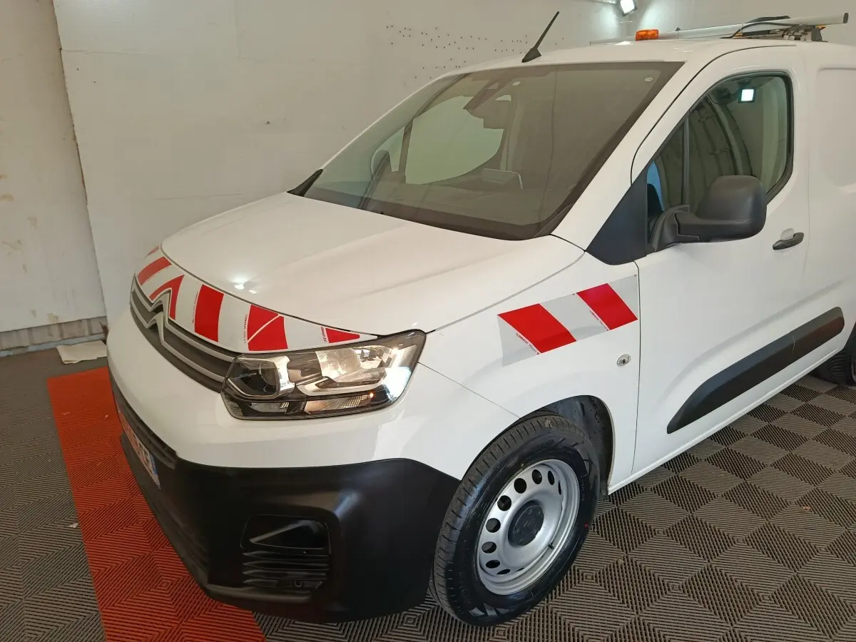 Vue 3/4 avant droit d'un Citroën Berlingo blanc 2021 avec bandes rouges et blanches réfléchissantes sur le capot et l'aile.