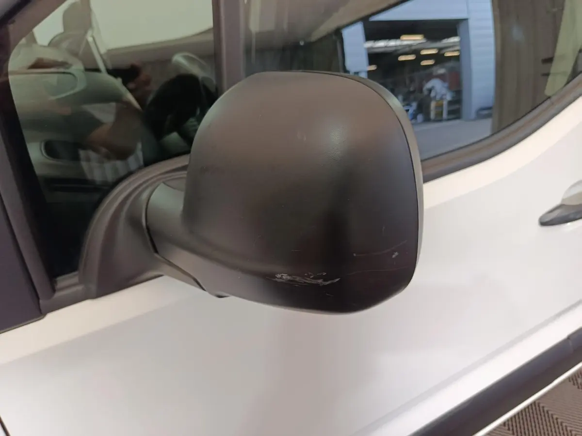 Gros plan sur le rétroviseur noir côté gauche d'un Citroën Berlingo blanc 2021 avec une rayure visible.