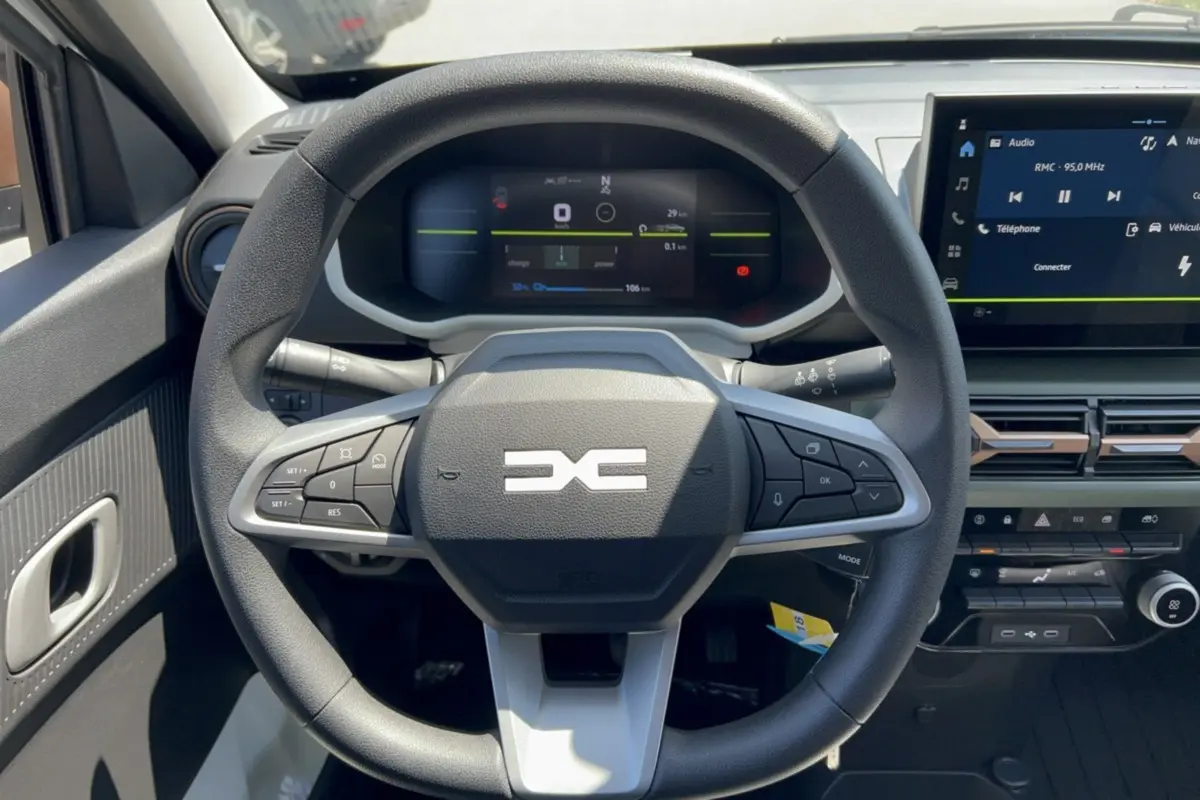 Vue frontale du volant et tableau de bord numérique du Dacia Spring électrique gris éclair avec écran tactile central.