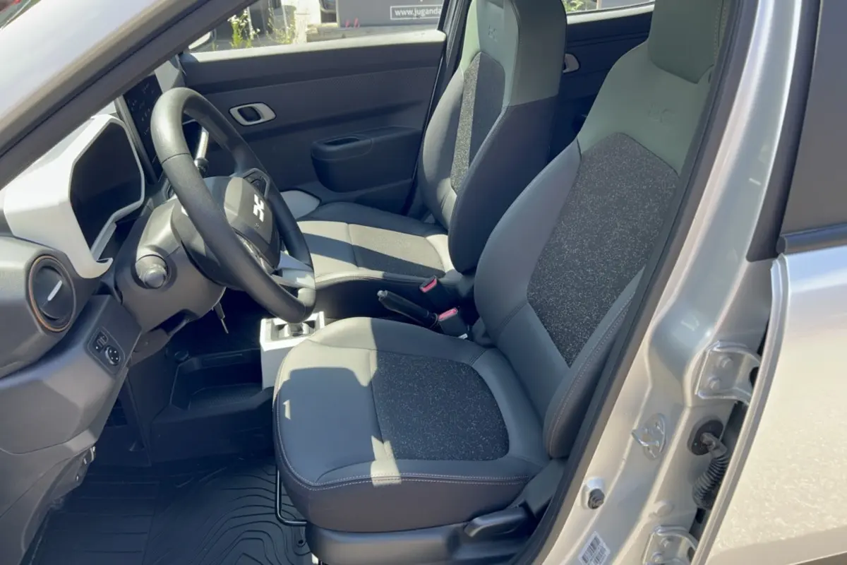 Vue intérieure côté conducteur de la Dacia Spring électrique gris éclair, avec sièges bi-matière cuir tissu et volant noir.