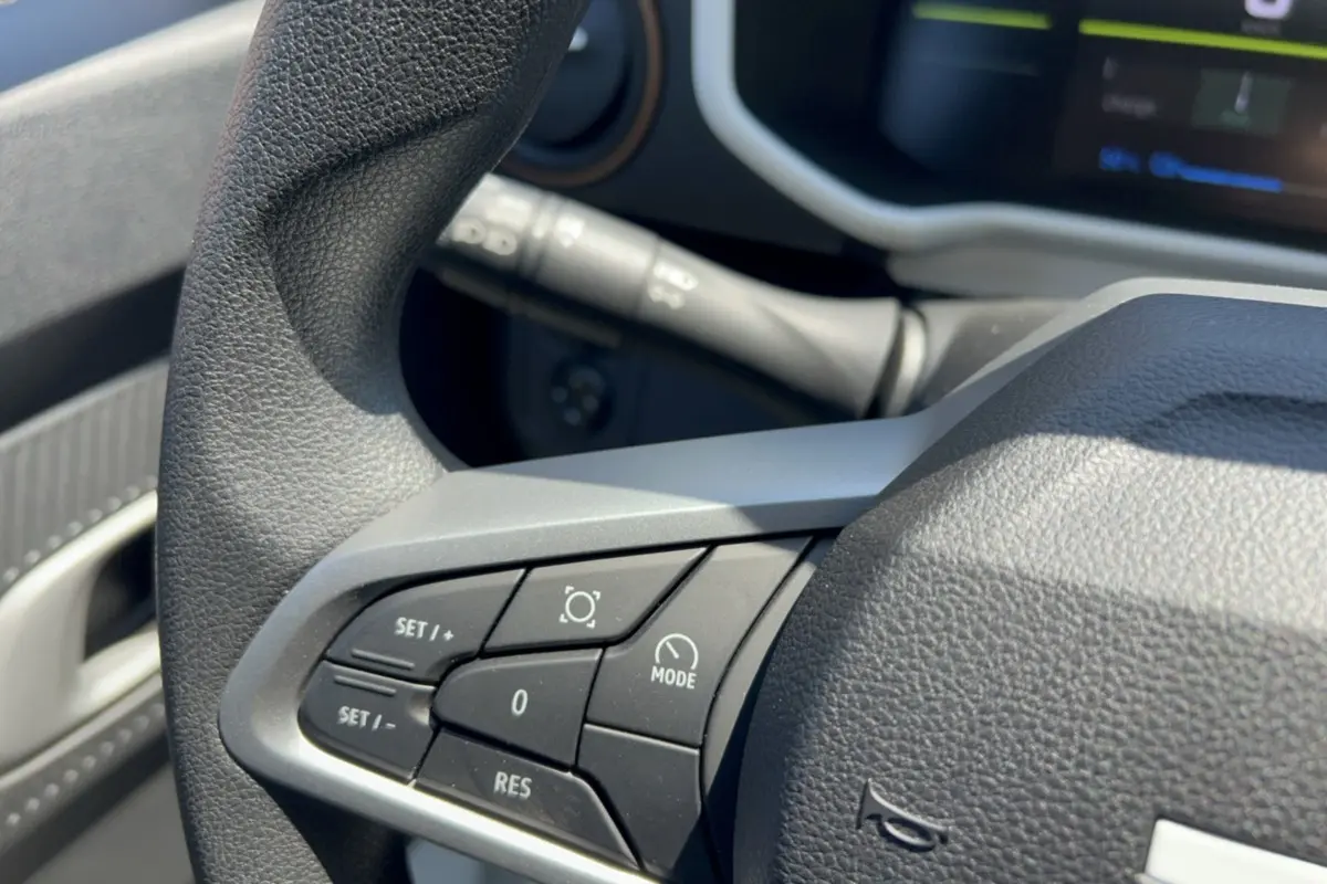 Gros plan sur les commandes au volant du Dacia Spring électrique 65 Extreme, avec tableau de bord numérique en arrière-plan.