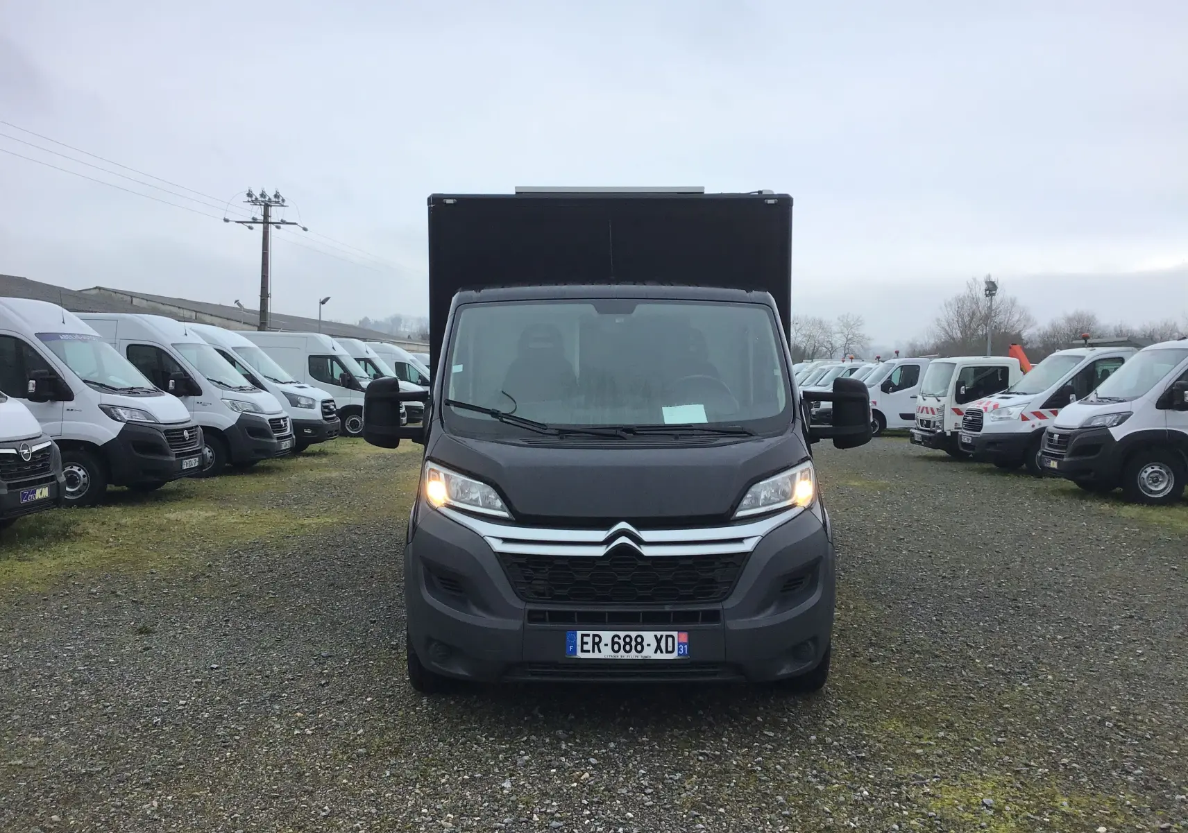 Vue frontale d'un Citroën Jumper plancher cabine gris graphito avec caisse magasin noire et feux allumés.