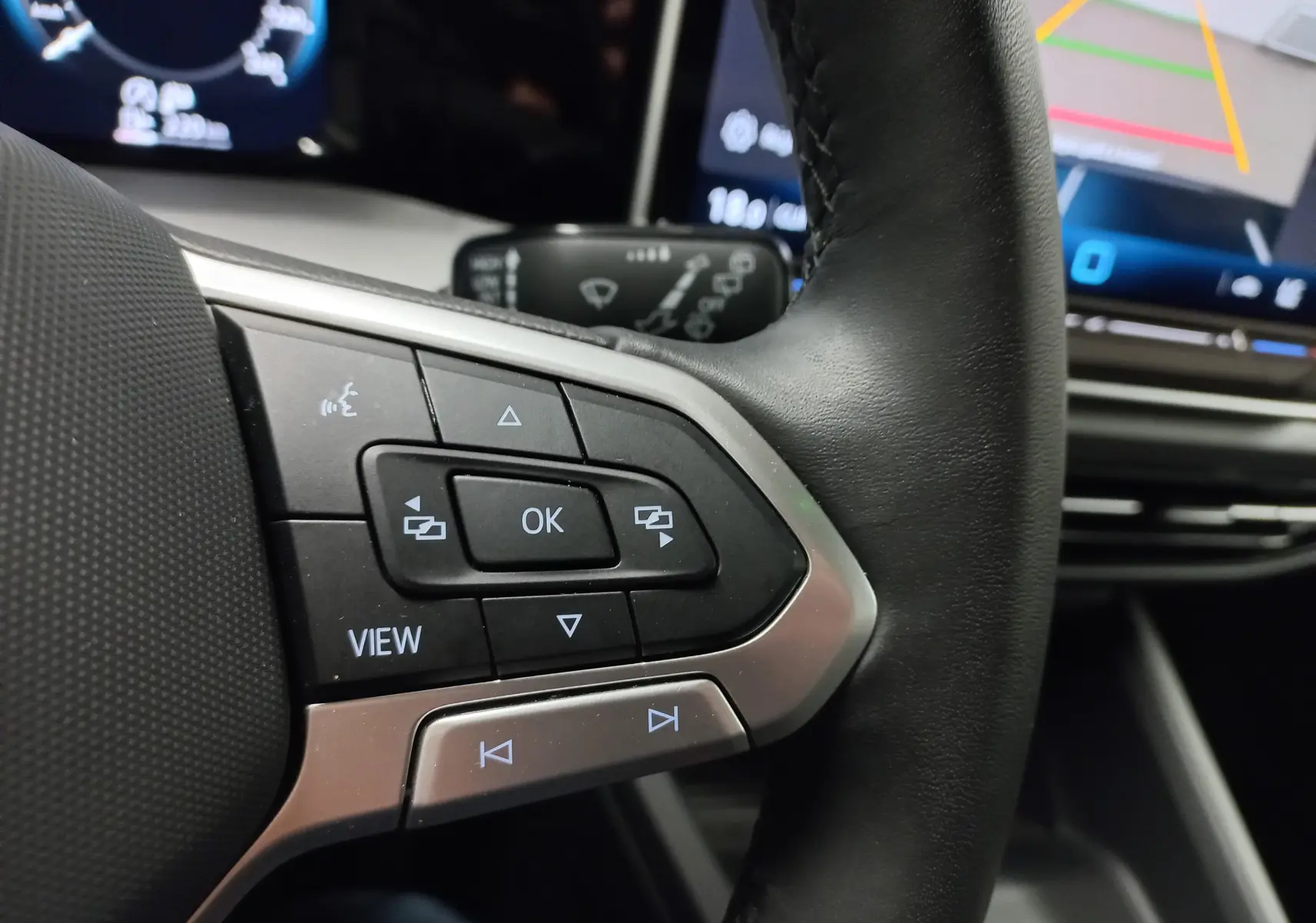 Gros plan sur les commandes au volant à gauche d'une Volkswagen Golf 1.5 TSI 2025 avec écran numérique en arrière-plan.